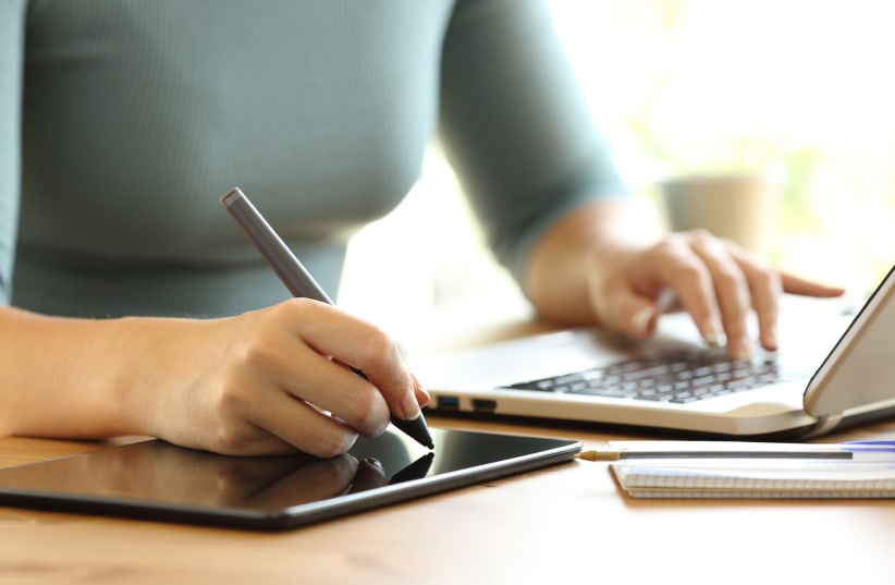 Close up of a woman hands working with a laptop and drawing in a digital tablet on a dek at home or office (Illustrative) (photo credit: INGIMAGE)