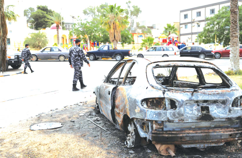 LIBYAN POLICEMEN walk past a destroyed car in Tarhouna, Libya, last week. (photo credit: ISMAIL ZITOUNY/ REUTERS)