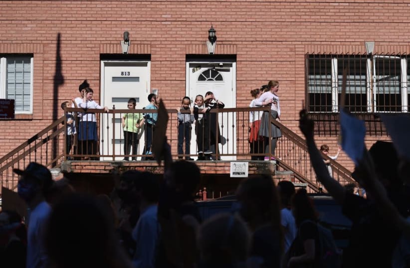 Orthodox children watch as protesters march through Brooklyn, June 3, 2020. Some yeshivas have provided instructions for parents to bring their children back to yeshiva three months after schools closed due to the pandemic (photo credit: ANGELA WEISS/GETTY IMAGES/JTA)