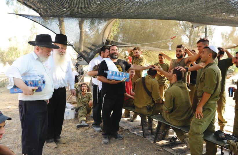 CHABAD EMISSARIES engage with IDF soldiers, offering to lay tefillin, at a staging area near the border with Gaza during Operation Protective Edge in July 2014. (photo credit: MENDY HECHTMAN/FLASH90)
