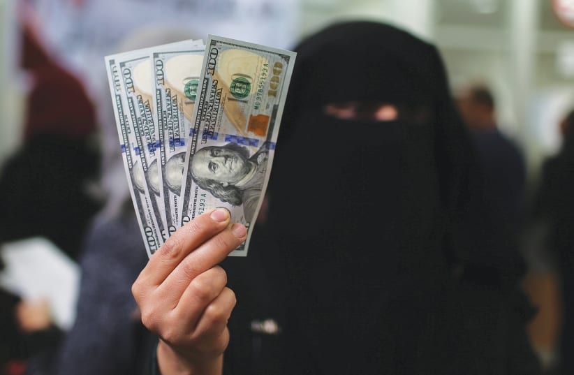 A HAMAS CIVIL servant in Gaza displays US dollar banknotes after receiving her salary paid by Qatar, in December 2018. (photo credit: IBRAHEEM ABU MUSTAFA/REUTERS)
