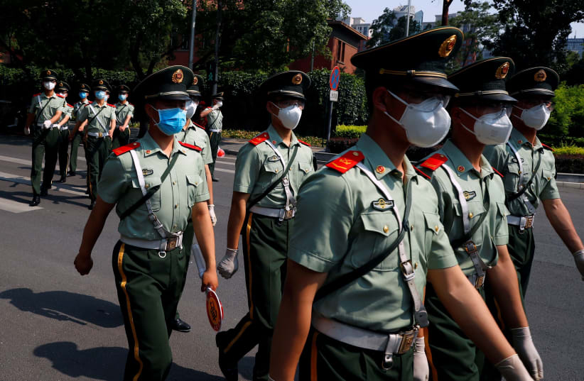 Paramilitary Police officers cross a street in the diplomatic district near a nucleic acid testing site, after a new outbreak of the coronavirus disease (COVID-19) in Beijing, China, June 19, 2020 (photo credit: THOMAS PETER/REUTERS)