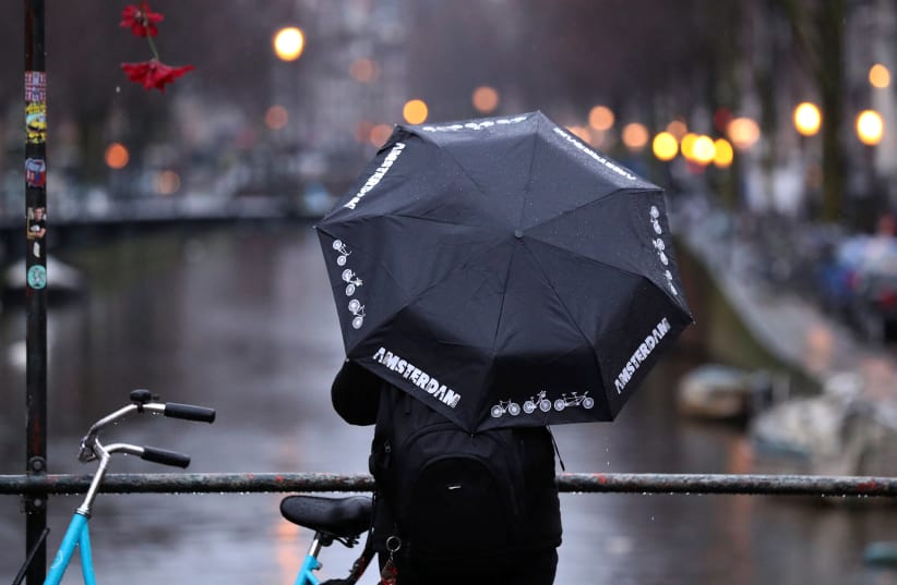 A man holds an umbrella while standing next to a canal in central Amsterdam, Netherlands March 2, 2020 (photo credit: YVES HERMAN/REUTERS)