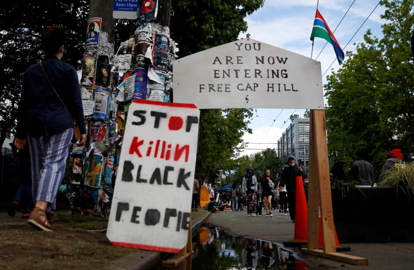 People walk by signs at a barrier set up at the edge of the self-proclaimed CHAZ/CHOP zone around the Seattle Police Department's East Precinct. June 14, 2020 (photo credit: REUTERS/LINDSEY WASSON)