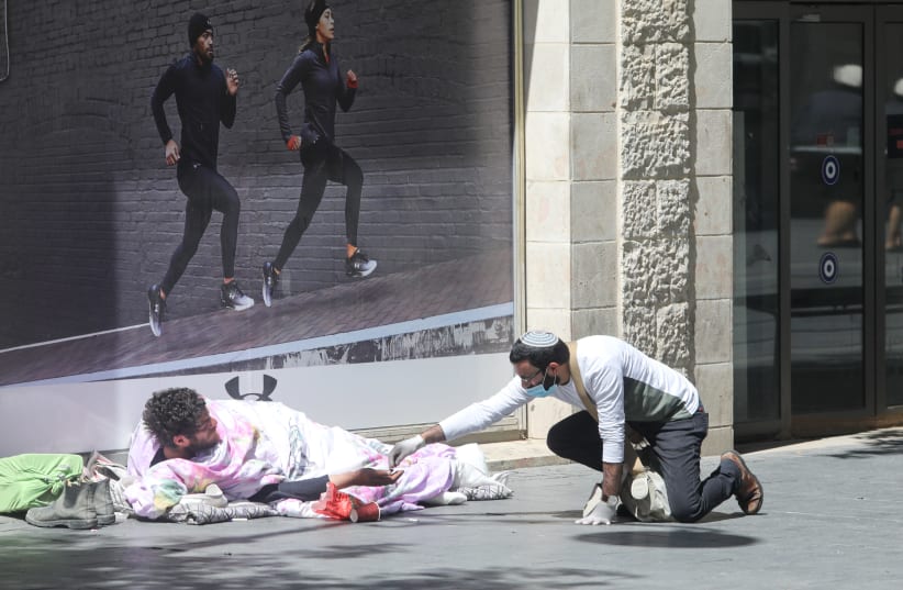 A masked man gives money to a homeless person at Jerusalem’s Mamilla Mall (photo credit: MARC ISRAEL SELLEM)