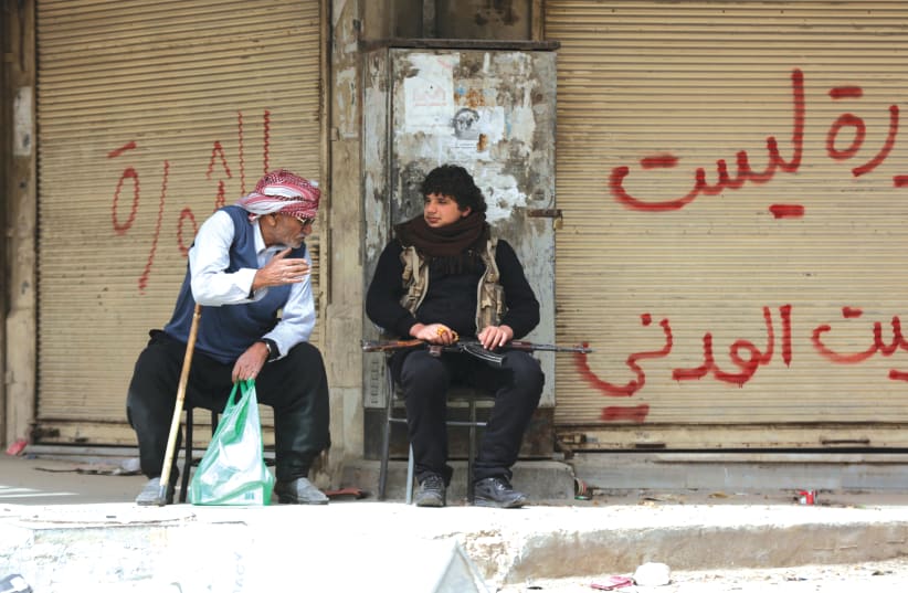 MEN TALK in front of closed shops in Afrin, Syria, in 2018. (photo credit: KHALIL ASHAWI / REUTERS)