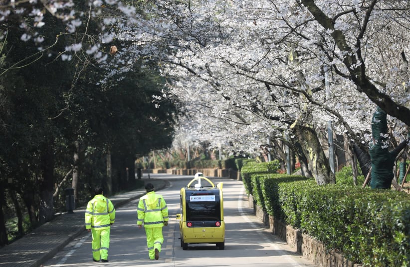 SECURITY PERSONNEL accompany a 5G-enabled autonomous vehicle, installed with a camera filming blooming cherry blossoms for an online live-streaming session, inside Wuhan University, Hubei province, China, on March 17. (photo credit: REUTERS)