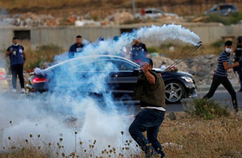 A Palestinian demonstrator returns a tear gas canister as a car carrying a bride and groom passes by during a protest against Israel's plan to annex parts of the West Bank, near the Beit El settlement. July 1, 2020. (photo credit: REUTERS/MOHAMAD TOROKMAN)