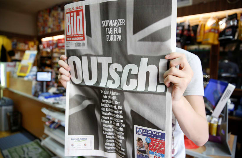A man holds up the German newspaper Bild with the titel "OUTsch!", for the camera, in Berlin, Germany, June 25, 2016 (photo credit: AXEL SCHMIDT/REUTERS)