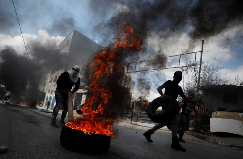 A demonstrator moves a tire during an anti-Israel protest following the funeral of Palestinian man Ibraheem Yakoub, in Kifl Haris in the West Bank July 10, 2020 (photo credit: REUTERS/MOHAMAD TOROKMAN)