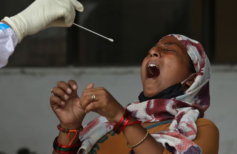 A woman reacts as a healthcare worker takes a swab from her to test for the coronavirus disease (COVID-19) in Kolkata, India July 10, 2020. (photo credit: REUTERS)