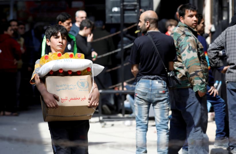 A boy holds a cardboard box of food aid received from World Food Programme in Aleppo's Kalasa district, Syria, April 10, 2019 (photo credit: REUTERS/OMAR SANADIKI)