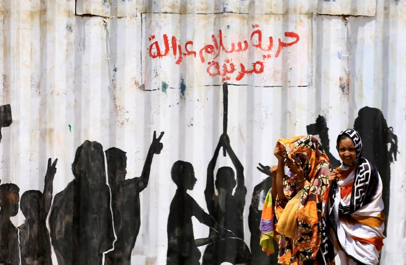 Civilians walk past graffiti reading in Arabic "Freedom, Peace, Justice and Civilian" in the Burri district of Khartoum, Khartoum, Sudan, July 10, 2019. (photo credit: REUTERS/MOHAMED NURELDIN ABDALLAH)