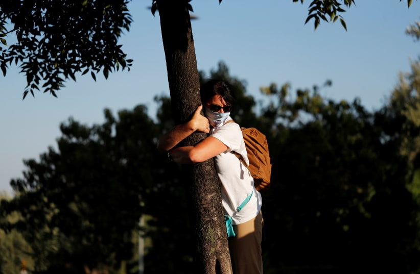 A woman takes part in a campaign by Israel's Nature and Parks Authority calling on people to join sightseeing tours and find comfort in tree hugging amid a spike in the coronavirus disease (COVID-19), in Jerusalem July 9, 2020 (photo credit: REUTERS/RONEN ZEVULUN)