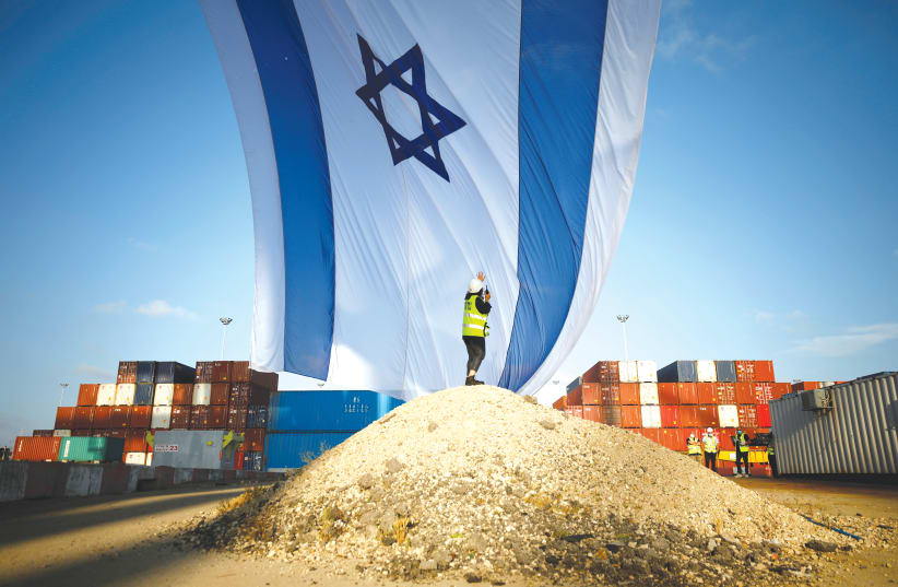 A WORKER at Ashdod port coordinates a crane to hang a giant Israeli national flag. (photo credit: REUTERS/AMIR COHEN)