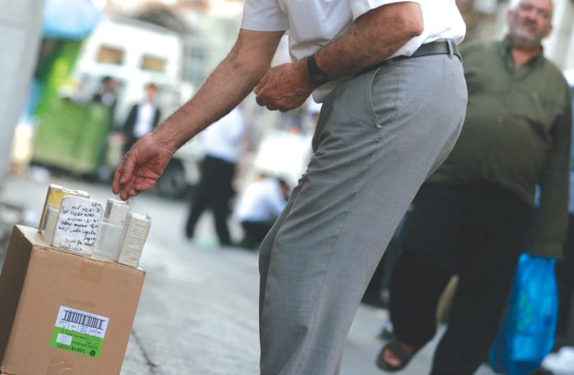 A man puts money into a charity box, in the streets of Mea She’arim in Jerusalem.  (photo credit: KOBI GIDEON/FLASH90)