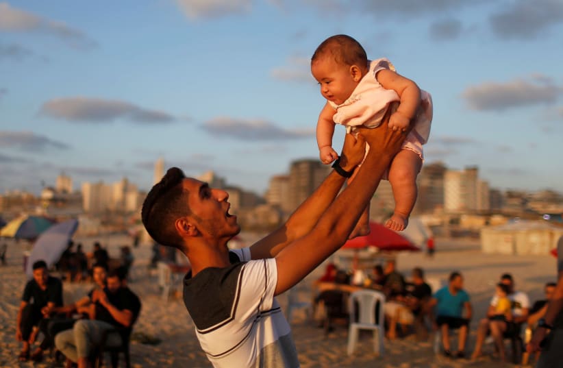 A Palestinian man lifts up his niece on a beach after the coronavirus disease (COVID-19) restrictions were largely eased, in Gaza City July 17, 2020. (photo credit: REUTERS/MOHAMMED SALEM)