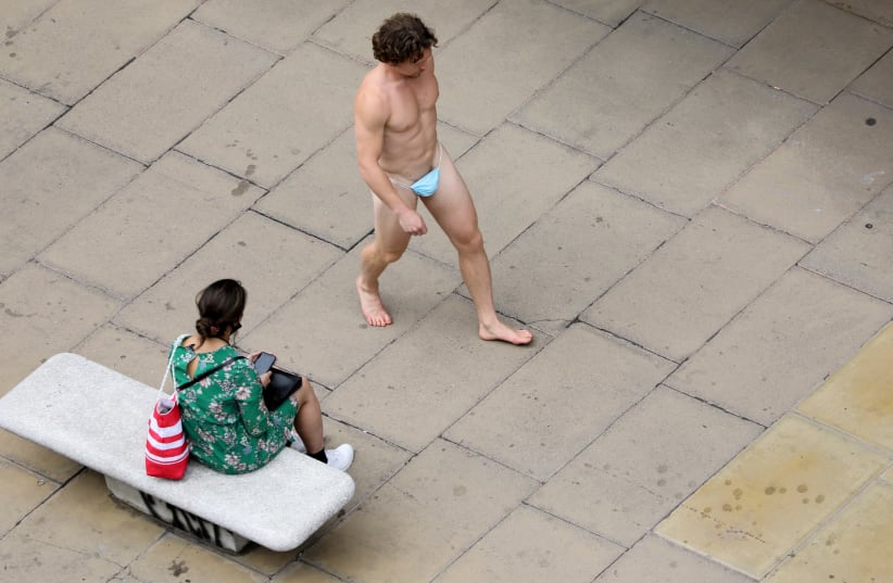 A man wearing a surgical mask as G-string walks past a woman, as the spread of the coronavirus disease (COVID-19) continues, on Oxford Street in London, Britain July 24, 2020 (photo credit: SIMON DAWSON/ REUTERS)