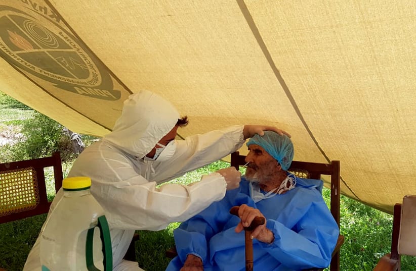 A paramedic wearing protective gear takes a nasal swab of 103 year-old Abdul Alim, to be tested for the coronavirus disease (COVID-19), at the Aga Khan Health Services Emergency Response Centre in Booni, Chitral, Pakistan in this undated photograph provided to Reuters (photo credit: SUHAIL AZIZ/HANDOUT VIA REUTERS)
