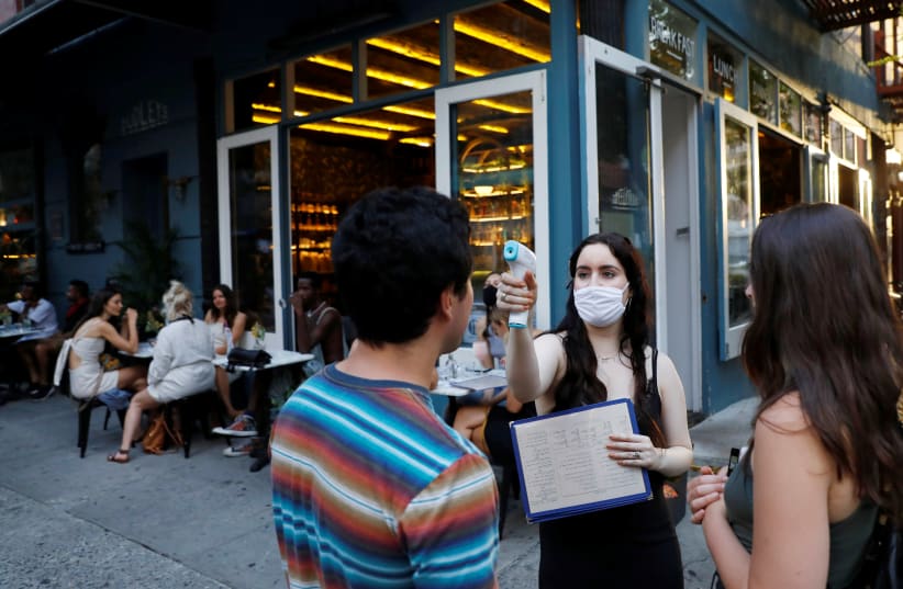 A waitress takes the temperature of customers as they arrive to eat at Dudley's as restaurants are permitted to offer al fresco dining as part of phase 2 reopening during the coronavirus disease (COVID-19) outbreak in the Lower East Side neighborhood of Manhattan in New York City, U.S., June 27, 202 (photo credit: REUTERS/ANDREW KELLY)