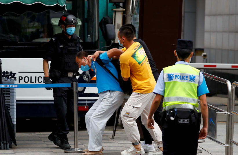 Plain clothes police officers detain a man who attempted to display a sign outside the US Consulate General in Chengdu, Sichuan province, China, July 25, 2020.  (photo credit: REUTERS)