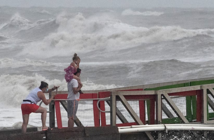 A girl covers her face from strong winds as her family members watch high swells from Hurricane Hanna from a jetty in Galveston, Texas, U.S., July 25, 2020. (photo credit: REUTERS/ADREES LATIF)