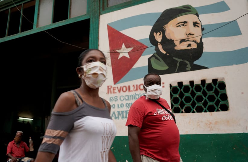 People pass by an image of late Cuban President Fidel Castro amid concerns about the spread of the coronavirus disease (COVID-19), in Havana, Cuba, July 19, 2020. (photo credit: ALEXANDRE MENEGHINI/ REUTERS)