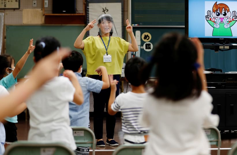 A teacher, wearing a protective face shield amid the coronavirus disease (COVID-19) outbreak, and students use sign language along with music instead of singing a song during the music class at Takanedai Daisan elementary school, which practices various methods of social distancing in order to preve (photo credit: REUTERS/KIM KYUNG-HOON)