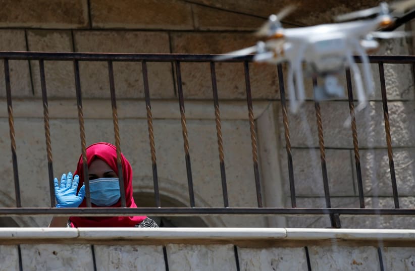 A Palestinian woman waves as she receives vitamins delivered by a drone in Beit Ummar in the West Bank on July 20 (photo credit: MUSSA QAWASMA / REUTERS)