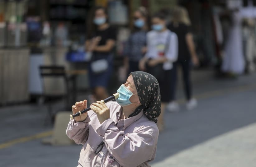 A woman wearing a mask plays a melancholy melody on her flute in downtown Jerusalem (photo credit: MARC ISRAEL SELLEM)