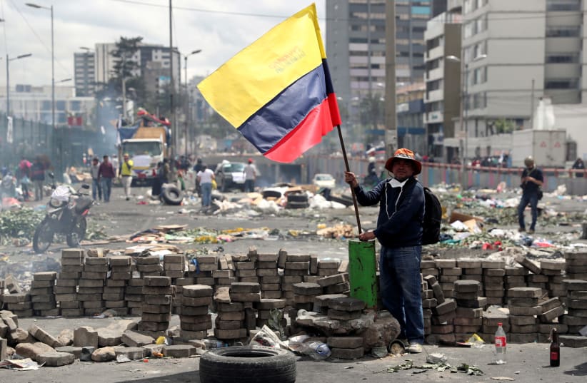 A man holds an Ecuadorian flag in the aftermath of protests against Ecuador's President Lenin Moreno's austerity measures, after Moreno imposed a military-enforced curfew in the capital Quito, Ecuador October 13, 2019. (photo credit: REUTERS)