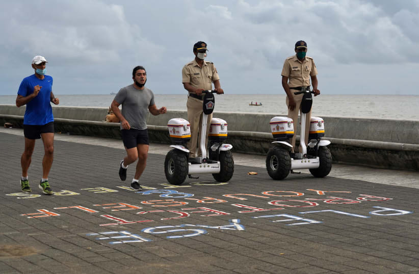 Police officers patrol on Segways as men wearing protective face masks run along the promenade at Marine Drive, after authorities eased lockdown restrictions that were imposed to slow the spread of the coronavirus disease (COVID-19), in Mumbai, India, June 12, 2020. (photo credit: REUTERS/HEMANSHI KAMANI)