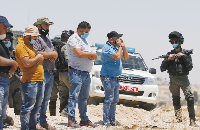 Palestinian demonstrators pray as an IDF soldier stands guard during a protest against Israel’s planned annexation, near Hebron, on July 17. (photo credit: MUSSA QAWASMA/REUTERS)