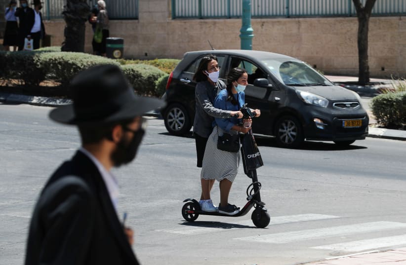 Israeli youths wearing masks ride a scooter as Israeli authorities brought back some coronavirus disease (COVID-19) restrictions after the number of new cases jumped in what officials fear could herald a "second wave" of infections, in Elad, Israel June 24, 2020 (photo credit: REUTERS/AMMAR AWAD)