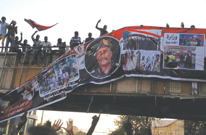 Protestors tear down a picture of Lt.-Gen. Abdel Fattah Al-Burhan Abdelrahman minutes after it was hung on a bridge in Khartoum, Sudan, in April 2019. (photo credit: UMIT BEKTAS / REUTERS)