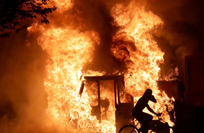 A man on a bike rides past a city truck on fire outside the Kenosha County Courthouse in Kenosha, Wisconsin, U.S., during protests following the police shooting of Black man Jacob Blake August 23, 2020. (photo credit: MIKE DE SISTI/MILWAUKEE JOURNAL SENTINEL VIA USA TODAY VIA REUTERS)