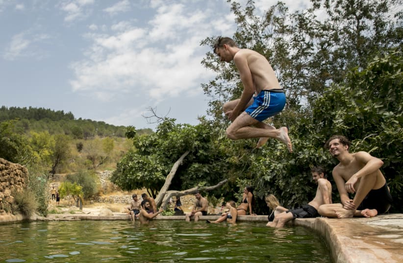 An Israeli man jump is seen jumping into water, as people enjoy a hot summer evening at the Ein Lavan Spring in Jerusalem, on July 27, 2020.  (photo credit: OLIVIER FITOUSSI/FLASH90)