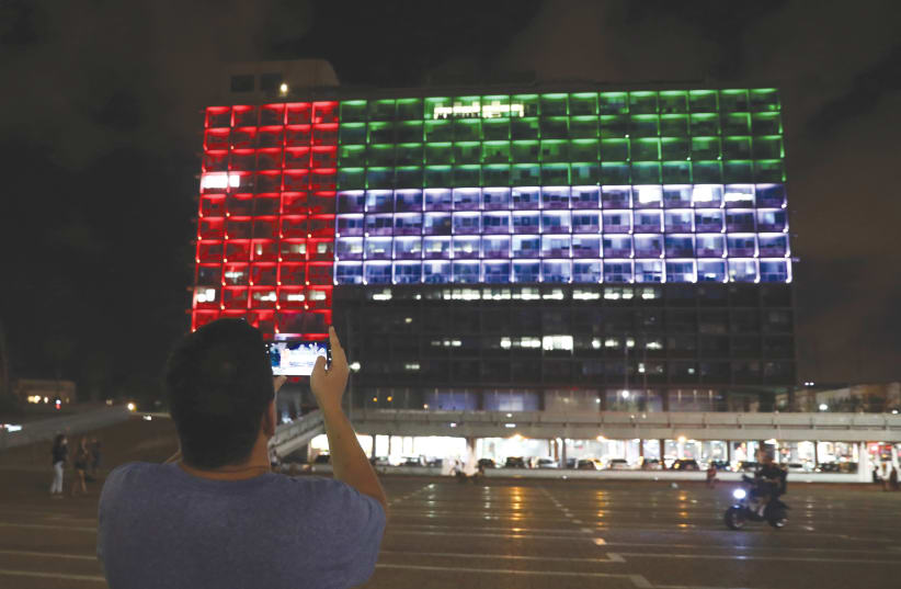 A MAN takes a picture as Tel Aviv City Hall is lit in the image of the United Arab Emirates national flag, following the announcement of a deal to normalize relations. (photo credit: AMMAR AWAD/REUTERS)