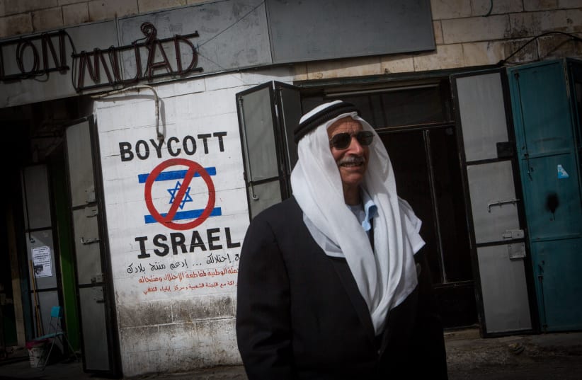 A Palestinian man walks by a grafitti sign calling to boycott Israel seen on a street in the West Bank city of Bethlehem on February 11, 2015. (photo credit: MIRIAM ALSTER/FLASH90)