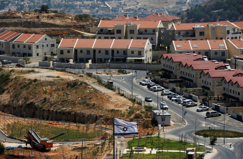 The Israeli national flag flutters as apartments are seen in the background in the Israeli settlement of Efrat in the West Bank August 18, 2020. (photo credit: RONEN ZVULUN/REUTERS)