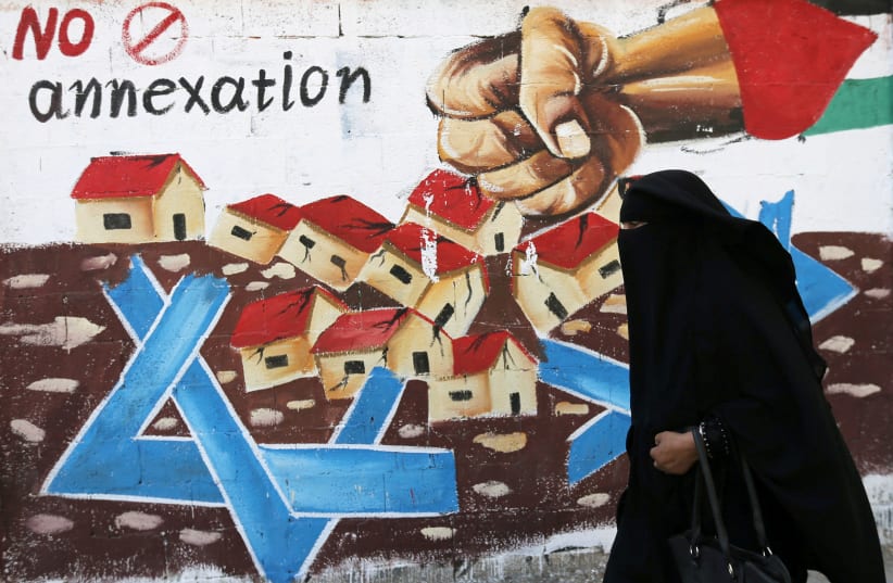 A Palestinian woman walks past a mural against Israel's plan to annex parts of the Israeli-occupied West Bank, in Rafah in the southern Gaza Strip July 14, 2020. (photo credit: IBRAHEEM ABU MUSTAFA/REUTERS)