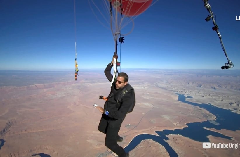 Extreme performer David Blaine hangs with a parachute under a cluster of balloons during a stunt to fly thousands of feet into the air in a still image from video taken over Page, Arizona, U.S. September 2, 2020 (photo credit: DAVID BLAINE/HANDOUT VIA REUTERS)