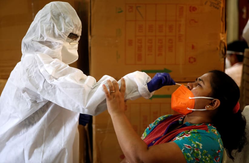 A health worker in personal protective equipment (PPE) collects a swab sample from a woman during a rapid antigen testing campaign for the coronavirus disease (COVID-19) in Mumbai, India, September 7, 2020 (photo credit: REUTERS/FRANCIS MASCARENHAS)