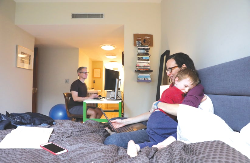 Naomi Hassebroek holds her son Felix while working with her husband, Doug Hassebroek, at their home, in Brooklyn, New York, in March 2020 (photo credit: CAITLIN OCHS/REUTERS)