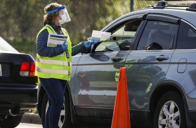  health care worker hands out testing information to people waiting at a drive-through COVID-19 testing site in Chicago, May 6, 2020 (photo credit: JOEL LERNER/XINHUA VIA GETTY/JTA)