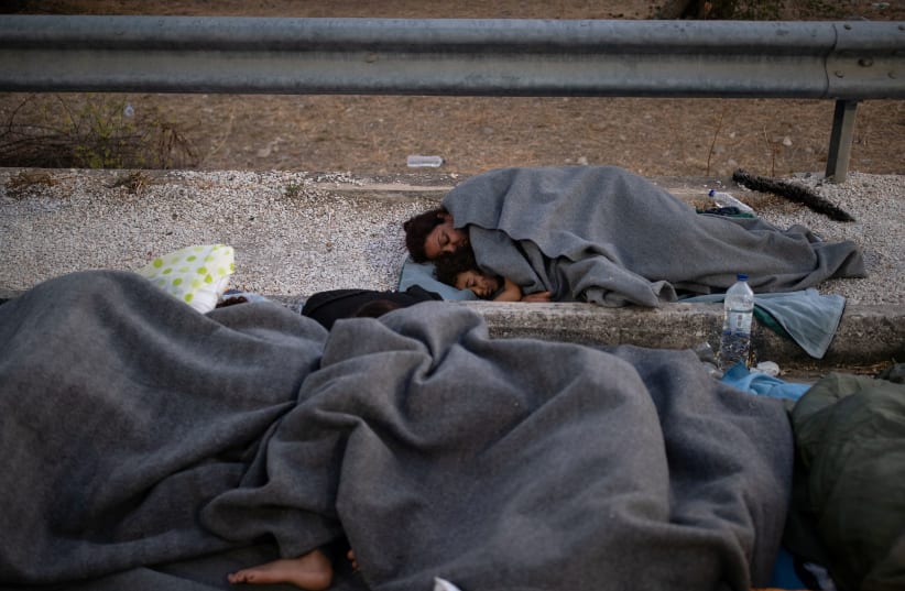 Refugees and migrants sleep on the side of a road following a fire at the Moria camp on the island of Lesbos. (photo credit: ALKIS KONSTANTINIDIS / REUTERS)