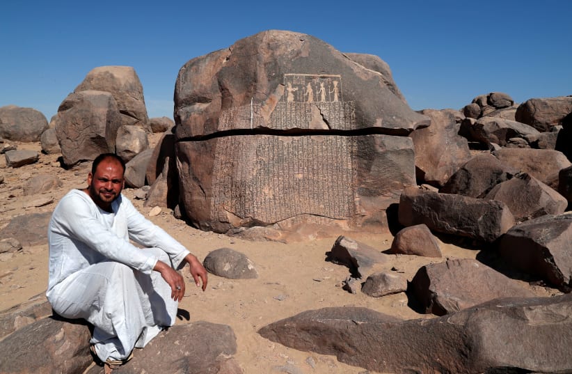 Ayman Hussien, a guard of Famine Stela, or "Rock of Starvation", sits near the rock, initially attributed to the reign of King Djoser (Third Dynasty), during a shortage of the Nile flood that led to a seven-year drought and famine, on the Nile's Sehel Island at Aswan, Egypt February 21, 2020 (photo credit: REUTERS/AMR ABDALLAH DALSH)