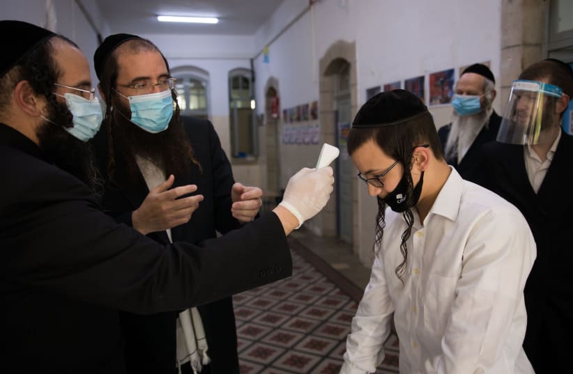 A teacher checks the temperature of a student at a haredi Orthodox school in Jerusalem, May 6, 2020 (photo credit: NATI SHOHAT/FLASH90)