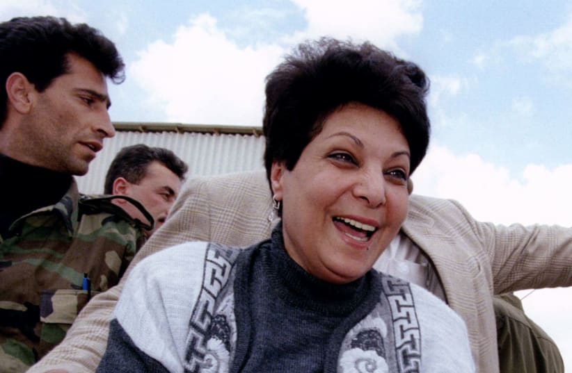 Leila Khaled, guarded by a Palestinian policeman (L), reaches for the hand of a supporter after crossing the Allenby Bridge April 18 1996 (photo credit: REUTERS)