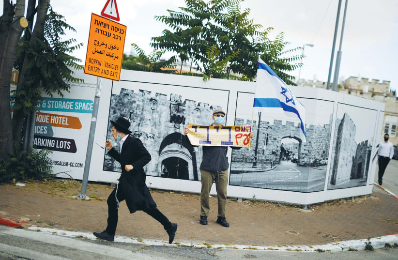 AN ULTRA-ORTHODOX man walks past a supporter of Prime Minister Benjamin Netanyahu holding a placard reading, ‘The nation is with Bibi,’ in May, 2020. (photo credit: AMIR COHEN/REUTERS)